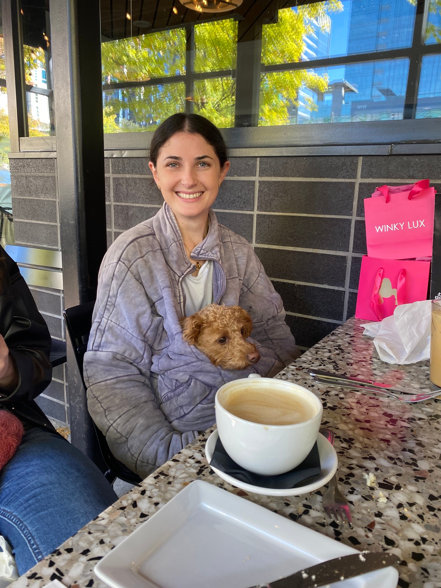 Ally smiling at a café with a small doodle in her arms
